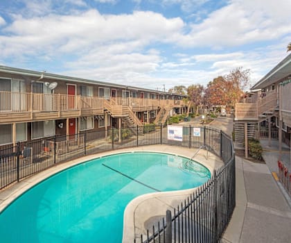 A swimming pool is surrounded by a black fence and apartment buildings.