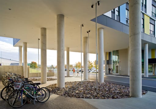 Exterior shot of Redstone Lofts; bike racks to left. Pool of decorative rocks to right with pillars supporting blue, yellow and white paneled building spread throughout.