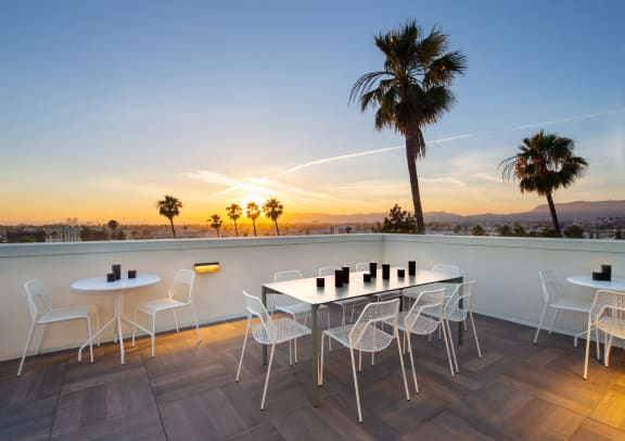 a terrace with a table and chairs overlooking a sunset and palm trees