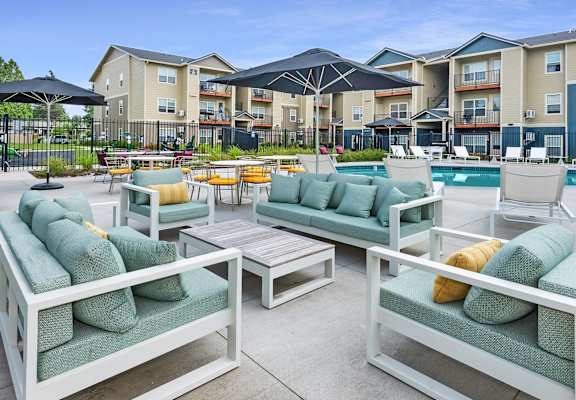 A poolside seating area with white furniture and green cushions.