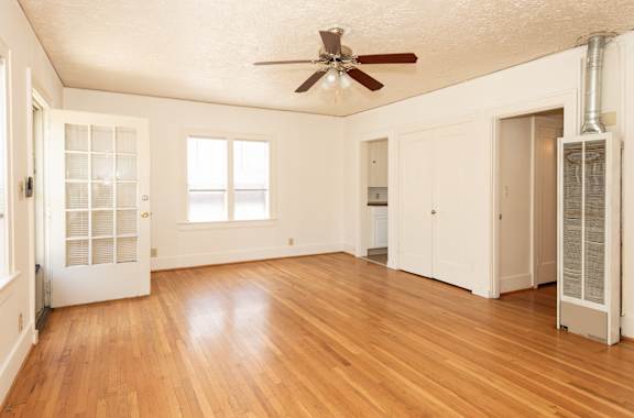 A room with a ceiling fan and wood flooring.