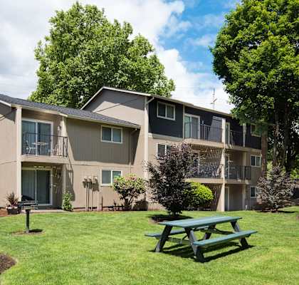 Exterior view of Cedar Lane & Garden Glen apartments with a picnic table on green grass.