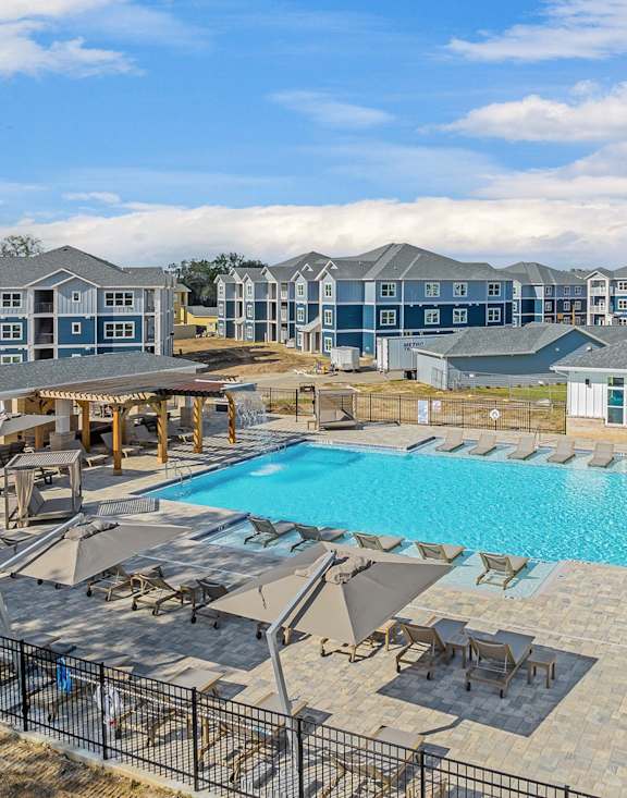 A large swimming pool surrounded by sun loungers and umbrellas with a building in the background.
