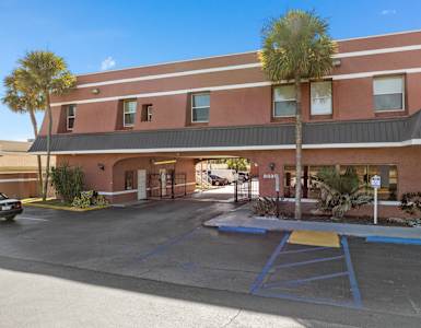 a red building with a parking lot and palm trees at Colonial Drive Apartments, Orlando, FL 32808