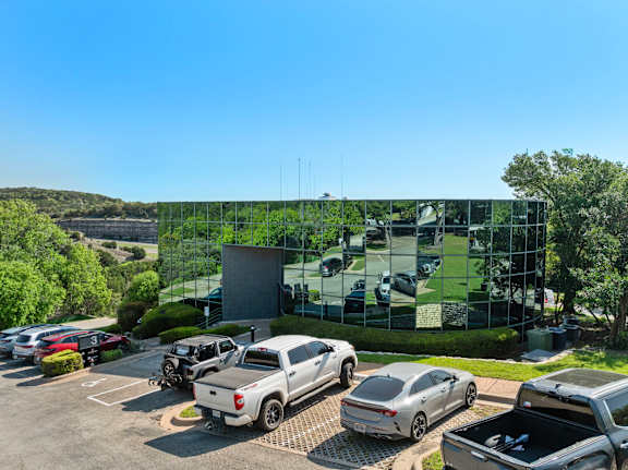 A parking lot with several cars and a building with a glass facade in the background.