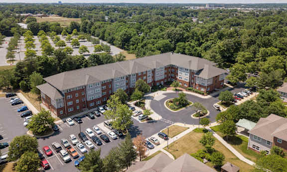 an aerial view of a large brick building with a gray roof and a parking lot with cars