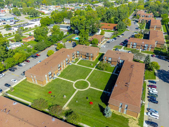 A large building with a red roof is surrounded by a green lawn and a circular garden.