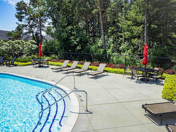 A pool surrounded by trees and chairs.