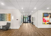 Thumbnail 1 of 8 - A hallway with a chair, a table, and a painting on the wall.