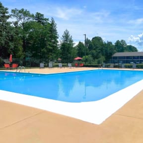 a swimming pool with chairs around it and trees in the background