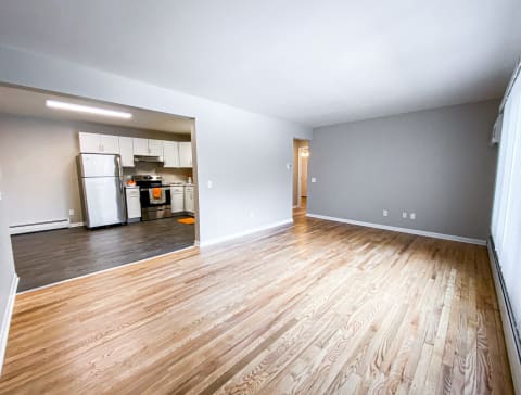 an empty living room with wood floors and a kitchen