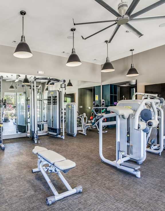 A spacious gym with a variety of equipment and a ceiling fan.