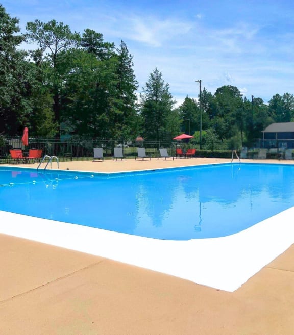 a swimming pool with chairs around it and trees in the background