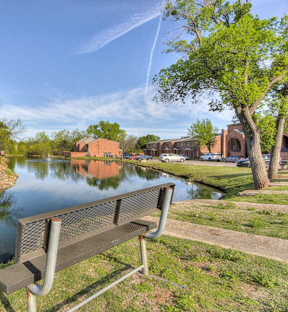 A park bench overlooks a calm body of water with a building in the distance.