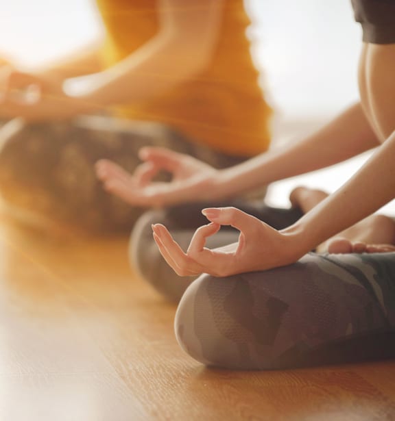 A group of people are sitting cross-legged on the floor in a yoga class.