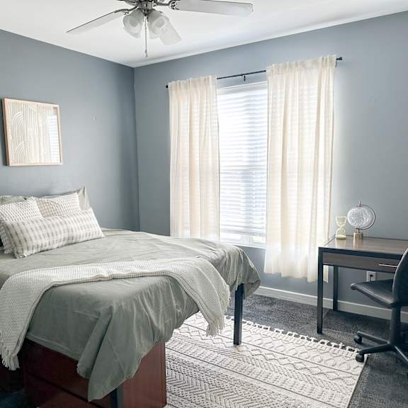 A bedroom with a bed, desk, chair, and ceiling fan.
