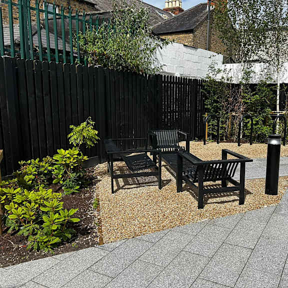 A black bench sits in a garden with a white wall in the background.