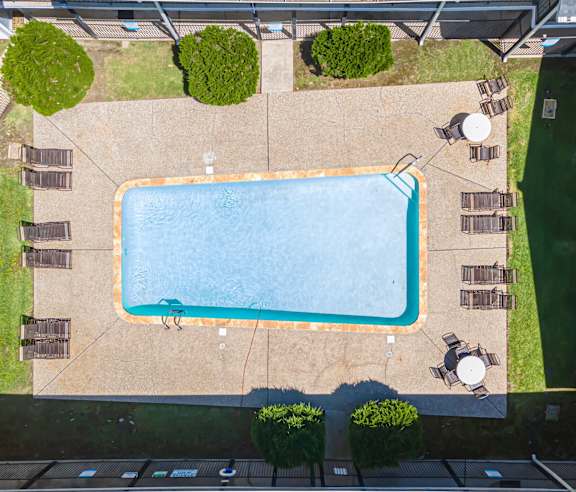 An aerial view of a swimming pool surrounded by a concrete patio and a grassy area.