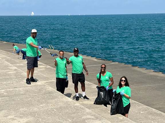 A group of people in green shirts are cleaning up trash by the sea.