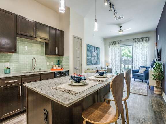 A kitchen with a marble countertop and wooden chairs.