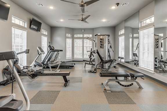 A spacious gym with a variety of equipment and a ceiling fan.