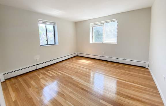 a bedroom with hardwood floors and two windows