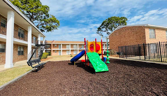 A playground with a green slide and a red and yellow slide in front of a building.