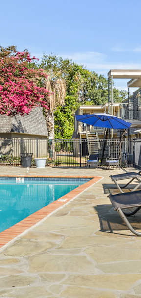 A pool surrounded by chairs and umbrellas with a building in the background.
