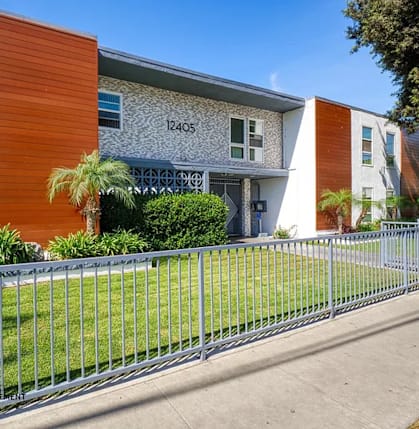 A modern building with a grey and orange facade and a metal fence in front.