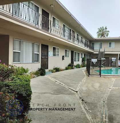 A courtyard with a pool and a fence in front of a building with balconies.