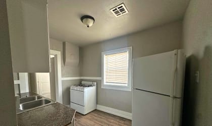 A kitchen with a white fridge, a window with blinds, and a washing machine.