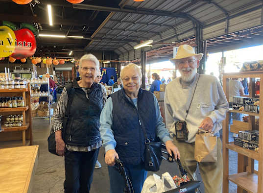 Three people are standing in a market with a man in the middle holding a bag.