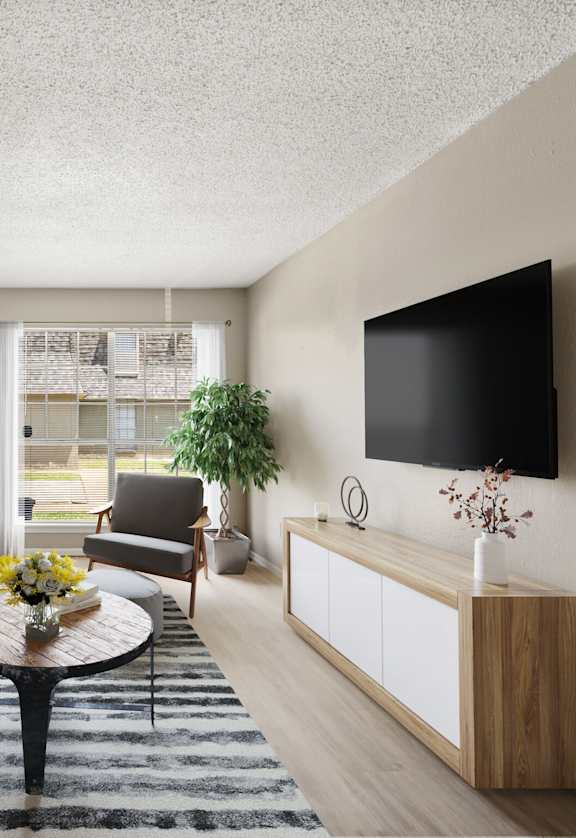 A living room with a grey couch, a coffee table, a chair, a plant, and a flat screen TV mounted on the wall.