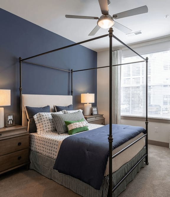 A bedroom with a four-poster bed, a ceiling fan, and a nightstand with a lamp.