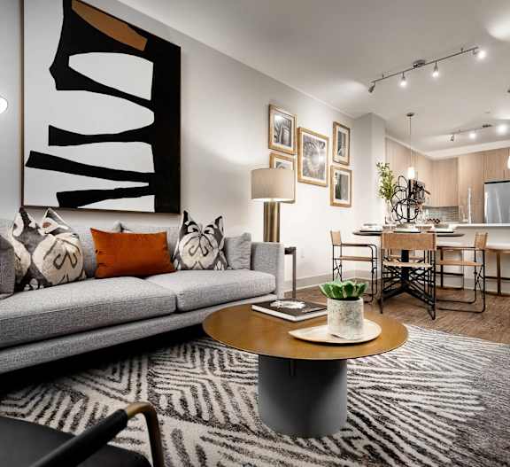 A modern living room with a grey couch, a coffee table, and a large abstract painting on the wall.