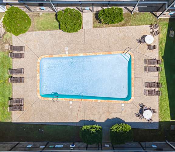 An aerial view of a swimming pool surrounded by a concrete patio and a grassy area.