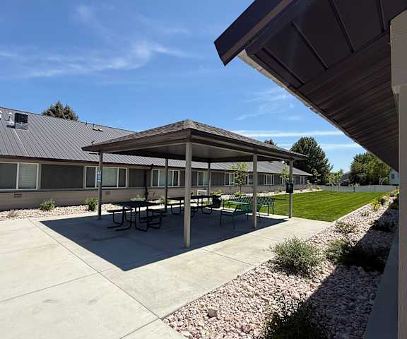 A covered picnic area with tables and benches is located in front of a building.