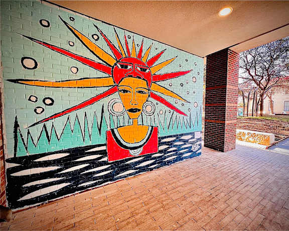 A mural of a woman with a sunburst behind her is painted on a wall.