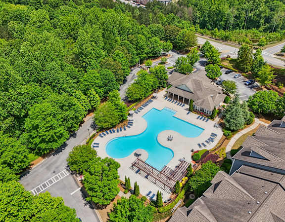An aerial view of a swimming pool surrounded by trees and a parking lot.