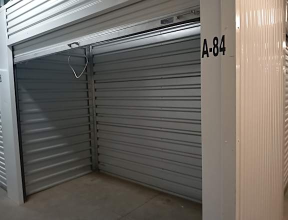 A closed grey shutter with a white handle and a white door with A-84 on it.