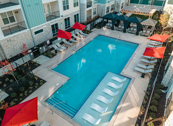 A swimming pool surrounded by red umbrellas and lounge chairs.