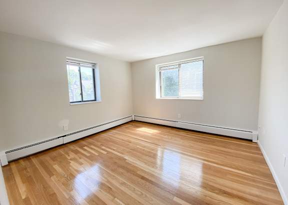 a bedroom with hardwood floors and two windows