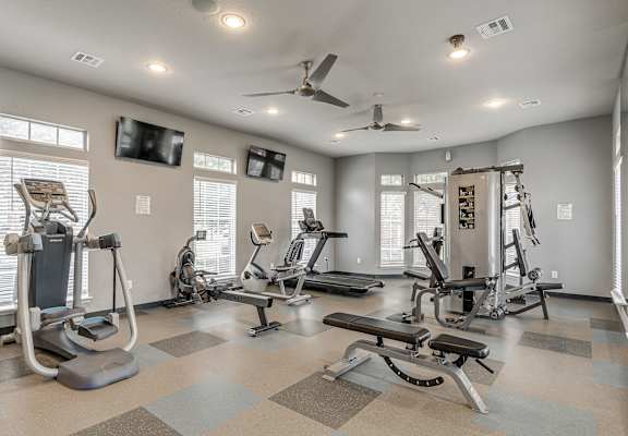 A spacious gym with a variety of equipment and a ceiling fan.