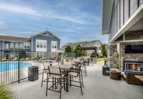 A patio with a table and chairs is surrounded by a pool and houses.