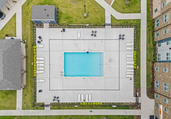 A swimming pool in the middle of a concrete area surrounded by grass and a few trees.