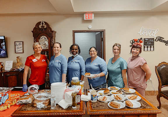 a group of women in blue t shirts stand in front of a table with food on it