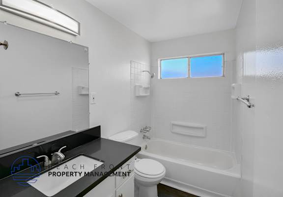 A white bathroom with a black counter top and a window.