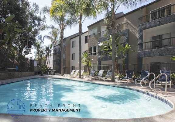 A pool surrounded by palm trees and chairs with the words "Beach Front Property Management" on the bottom left.