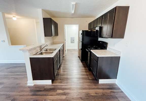 an empty kitchen with black appliances and wooden floors