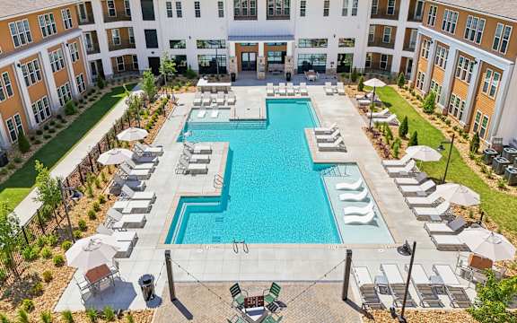 A large swimming pool surrounded by lounge chairs and umbrellas in a courtyard.